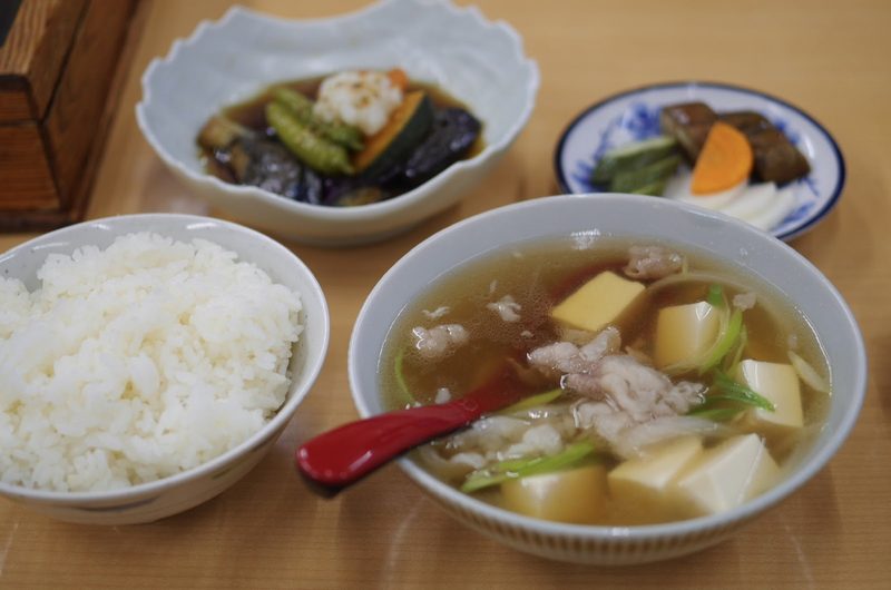 豆腐と肉、青ねぎが入った澄んだだしの汁物と、ご飯や小鉢